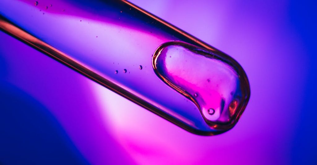 Close-up of liquid in a test tube against a vibrant purple and blue backdrop.