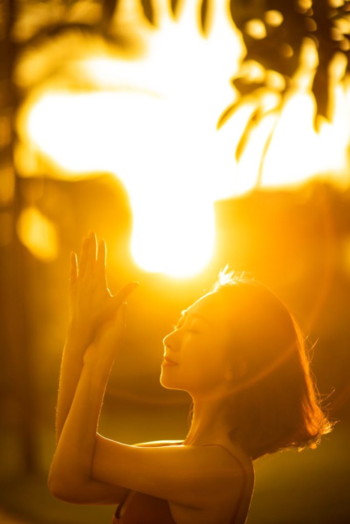 Asian woman practicing yoga at sunrise with a meditative pose, bathed in warm sunlight.