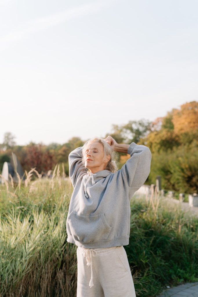 Elderly woman stretches outdoors in nature, embracing a healthy lifestyle and fitness.