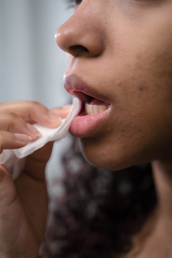 A close-up of a woman wiping her lips with a tissue, focusing on skincare and hygiene.