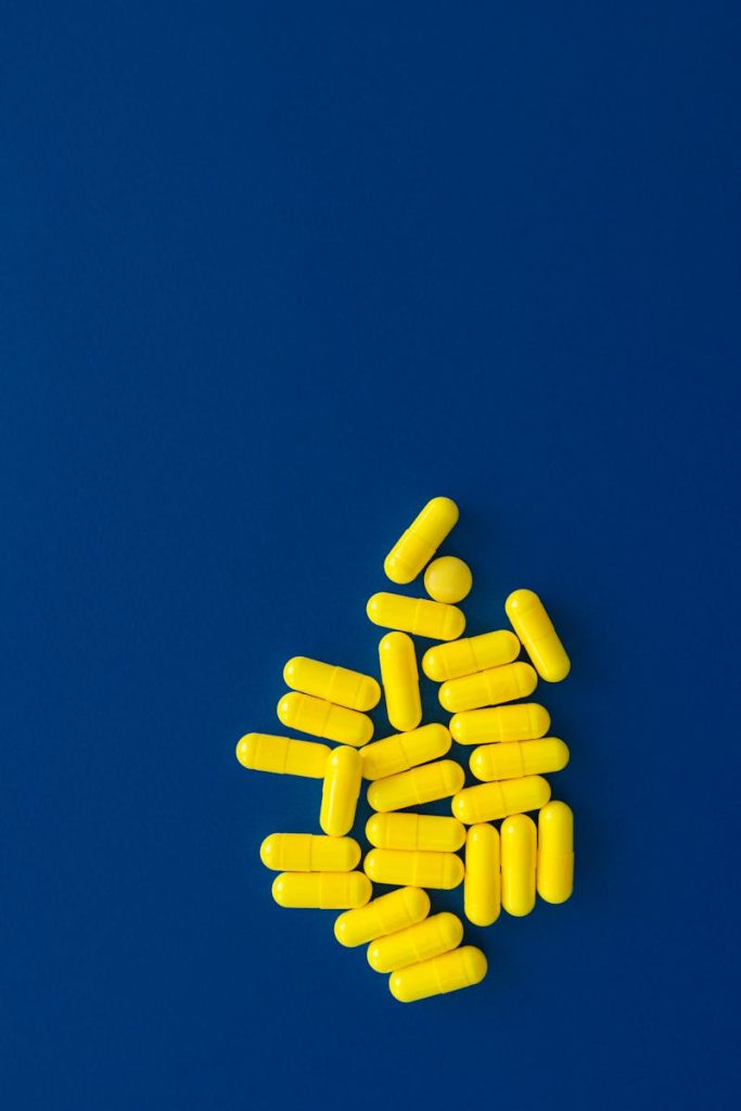 A flatlay of yellow capsules on a dark blue background, depicting healthcare and medicine.